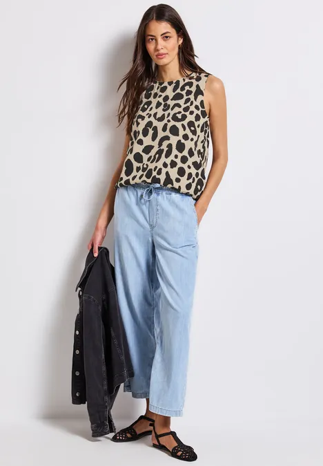 Frau mit Leo-Top, weitem Jeanshose und schwarzer Jacke in der Hand.